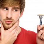 A young man rubbing his beard and looking at his razor.